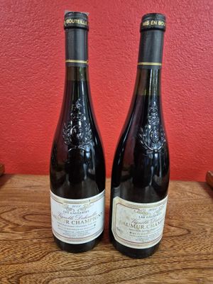 two bottles of wine sit on a table in front of a red wall