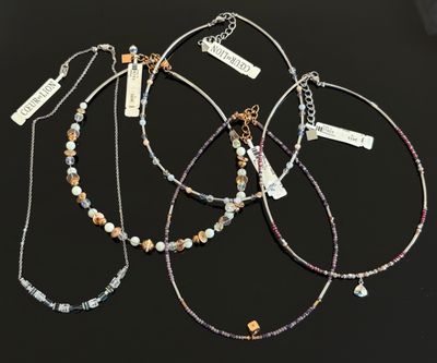 un lot de quatre colliers posés sur une table, accompagnés d'étiquettes