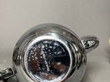 a silver tea pot and a silver cup on a table