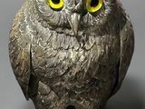 silver owl figurine with yellow eyes sitting on a gray surface
