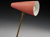 une lampe orange posée sur un trépied, devant un fond noir