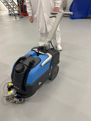 un homme vêtu d'une salopette blanche, debout à côté d'une machine bleue dans un entrepôt
