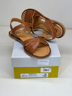 tan leather sandals with straps on top of a box on a white surface
