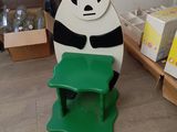 un panda assis sur un tabouret vert dans une pièce