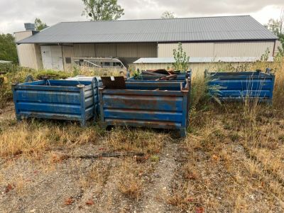 deux bennes bleues posées dans un champ à côté d'un bâtiment