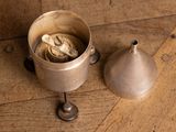 a small metal cup with a spoon and a metal bell on a wooden floor