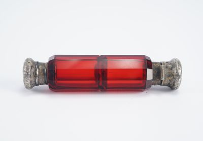 un gros plan d'une bouteille en verre rouge posée sur une surface blanche