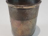 an old silver cup with a handle on a white surface