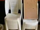 trois chaises en plastique blanc, avec un tableau en liège fixé au dossier