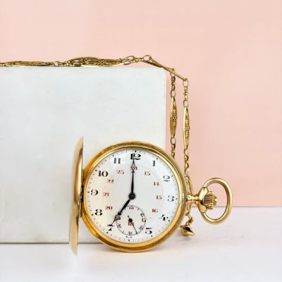 une montre de poche en or posée à côté d'une boîte blanche