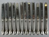 six silverplated knives and six spoons are lined up on a table