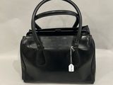 un sac à main noir muni d'une étiquette, posé sur une surface blanche