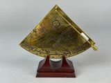 un cadran solaire en laiton posé sur un socle en bois, sur fond blanc