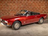 an image of a red convertible car parked in front of a brick wall
