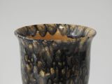 a close up of a black and gold vase on a white surface