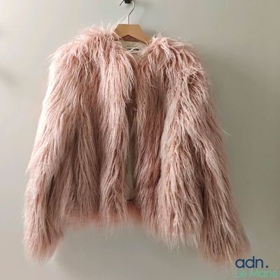 pink fluffy jacket hanging on a hanger against a wall