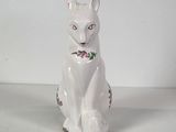 a white cat sitting on the floor with a flower on it ' s collar