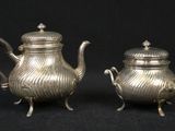 pair of antique silver teapots on stand on black background