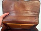 someone is holding a brown leather purse with a gold handle