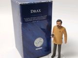 a toy figure of a man standing next to a box of drax
