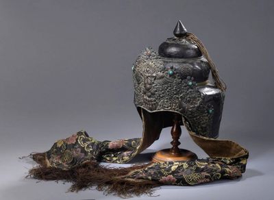un casque en argent et en or posé sur un socle, orné d'une longue chevelure