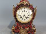 une horloge rouge et dorée posée sur une surface grise