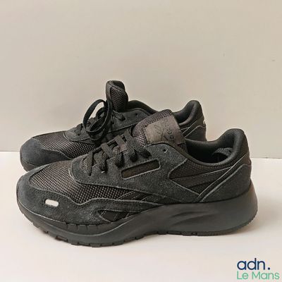 un gros plan sur une paire de baskets noires posées sur une surface blanche