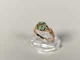 a close up of a gold ring with green stones on a clear surface