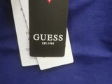 someone is holding a tag that says guess on it in front of a blue shirt