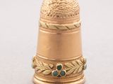 an image of a gold thimble with a green bead on it