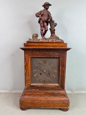 une horloge en bois surmontée d'une statue d'homme