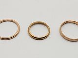 three gold wedding rings on a white surface