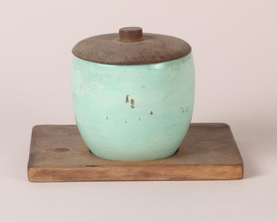 un petit pot vert muni d'un couvercle en bois, posé sur un socle en bois