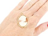 woman ' s hand with red manicured nails and a gold ring with a picture of a woman ' s face