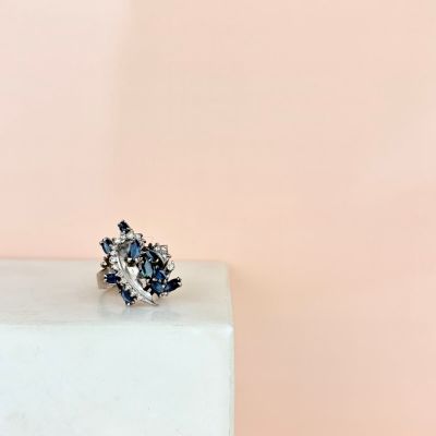 a close up of a diamond and sapphire cluster ring on a white marble block
