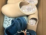 Plusieurs paires de Crocs se trouvent dans une boîte en carton posée par terre.