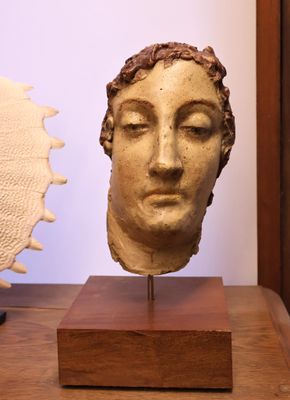 sculpture représentant une tête de femme, posée sur un socle en bois à côté d'un coquillage