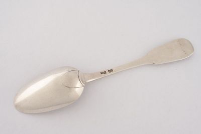 une cuillère en argent posée sur une surface blanche, avec une petite cuillère au milieu