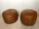 two brown leather ottomans sitting on top of a hard wood floor