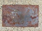 rusted metal plate on the ground with a piece of rust on it