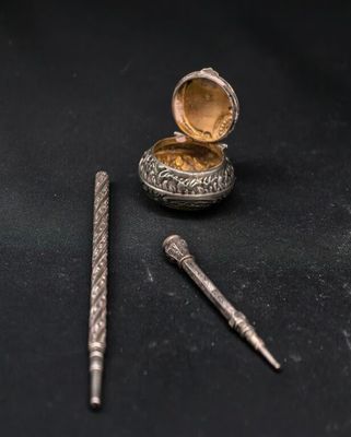 une petite boîte en argent, avec un stylo à côté, posée sur une surface noire