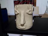 un vase blanc orné d'un visage, posé sur une étagère