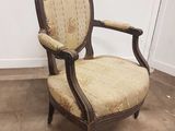une chaise à l'ancienne, dont le dossier et les accoudoirs sont recouverts d'un tissu à motifs floraux