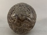 an old metal ball with carvings on it sitting on a white surface