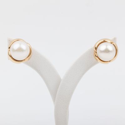 a pair of gold and pearl earrings on a white stand