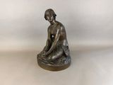 bronze statue of a woman sitting on a rock with her hands on her knees