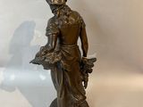 bronze statue of a woman holding a basket of flowers on a pedestal