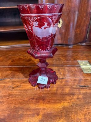 un vase rouge posé sur une table en bois, sur laquelle se trouve une étiquette