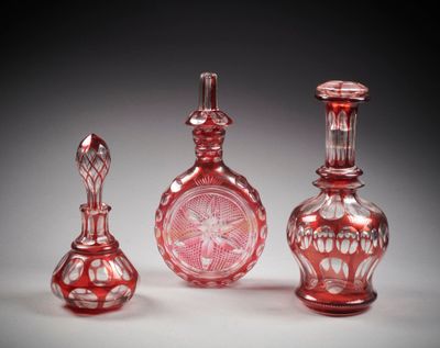 trois vases en verre rouge posés les uns à côté des autres sur une surface blanche