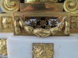 a gold clock on a white marble pedestal with gold decorations